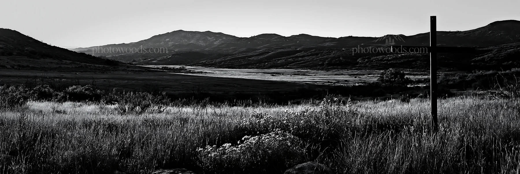 Iron Christian cross overlooking valley meadow in black and white - AI-generated stock image