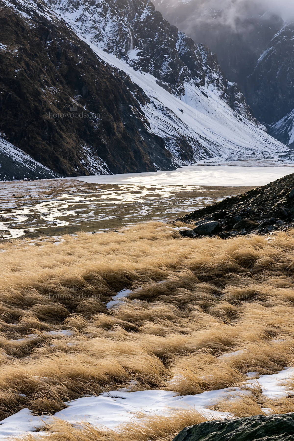 Frozen tarn meadow in mountain valley with grass and snow - AI-generated stock image