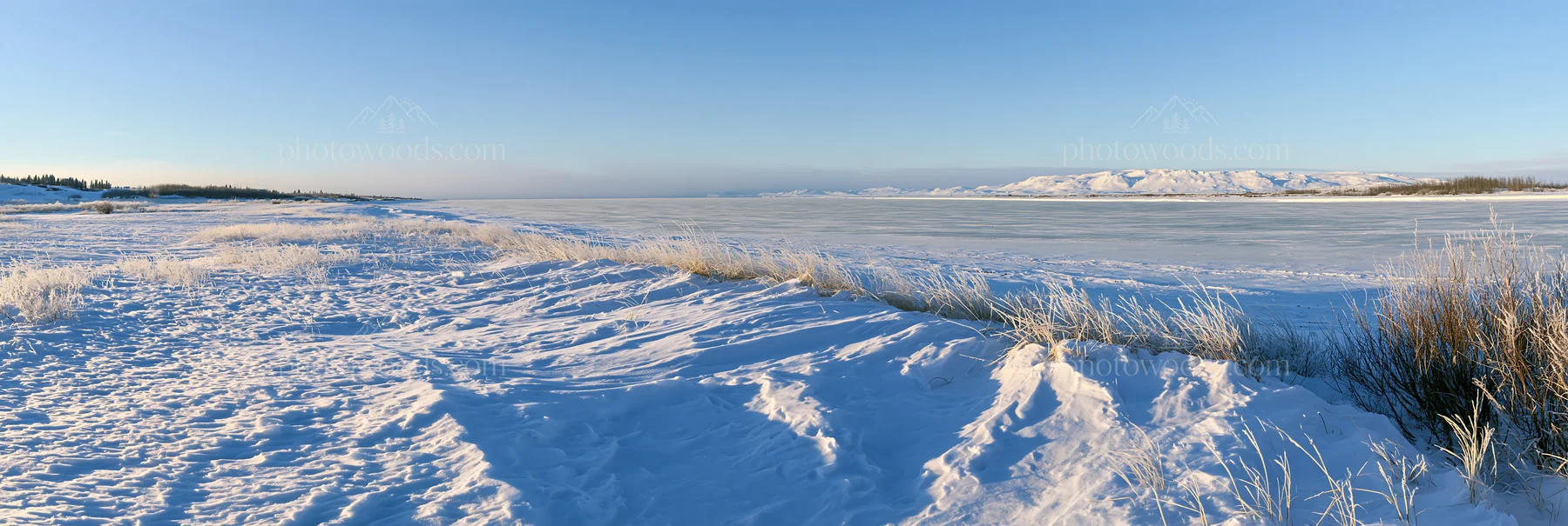 Snowy lakeside meadow with ice and distant hills - AI-generated stock image