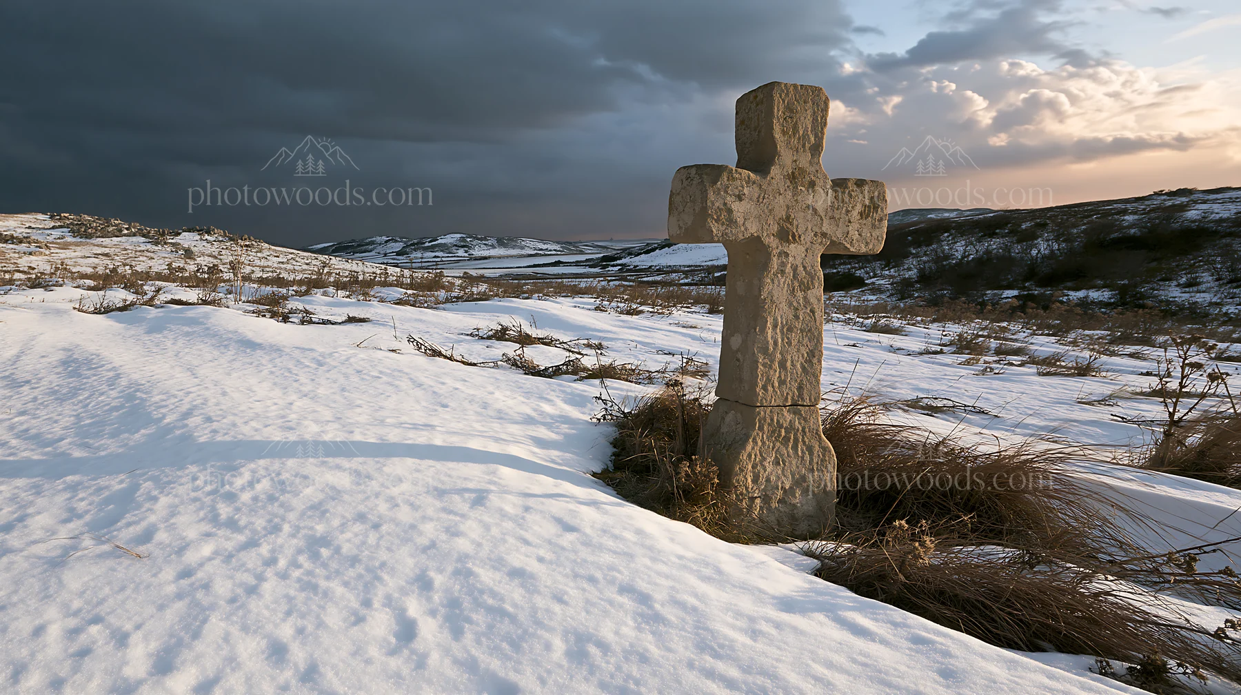 Stone Christian cross in snowy meadow at sunset - AI-generated stock image
