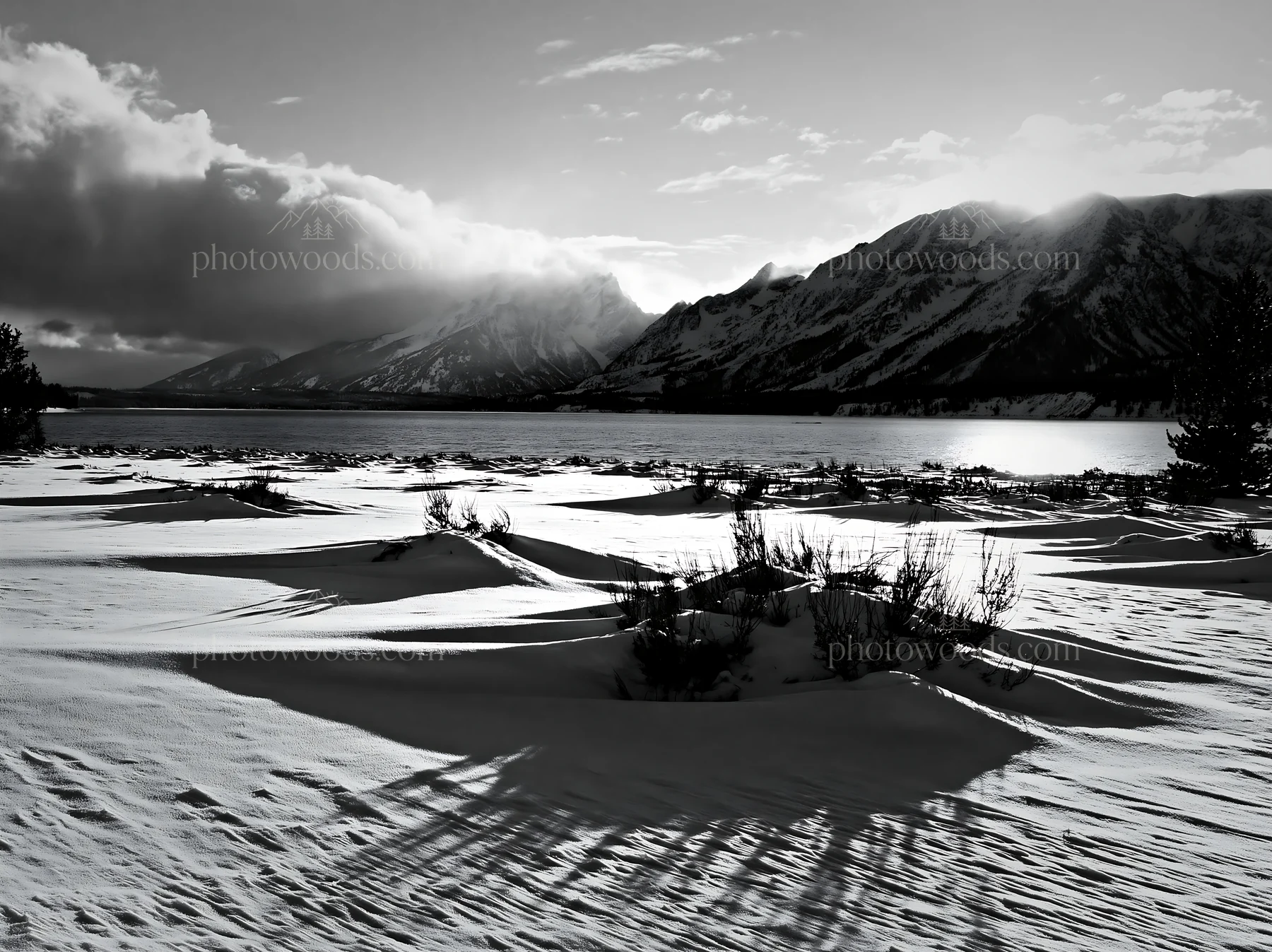 Black and white snowy lakeside meadow with mountains and sun in the background - AI-generated stock image