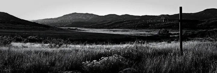 Iron Christian cross overlooking valley meadow in black and white - AI-generated stock image
