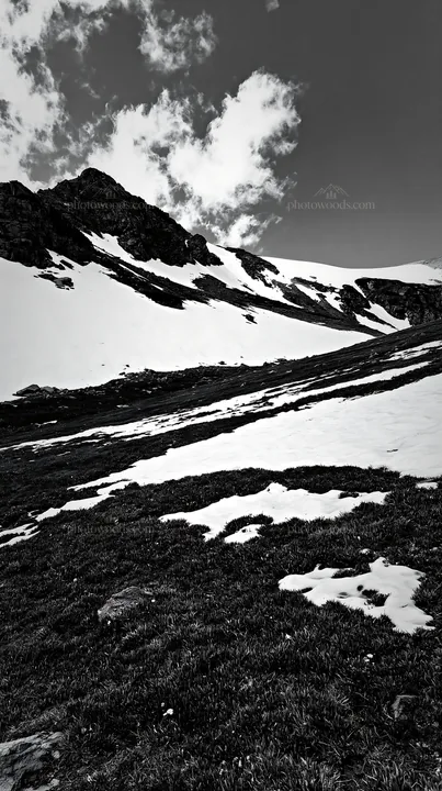 Mountain pass meadow with snow and rocky slopes - AI-generated stock image