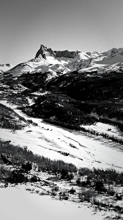 Black and white aerial view snowy meadow valley shows mountains in the background - AI-generated stock image