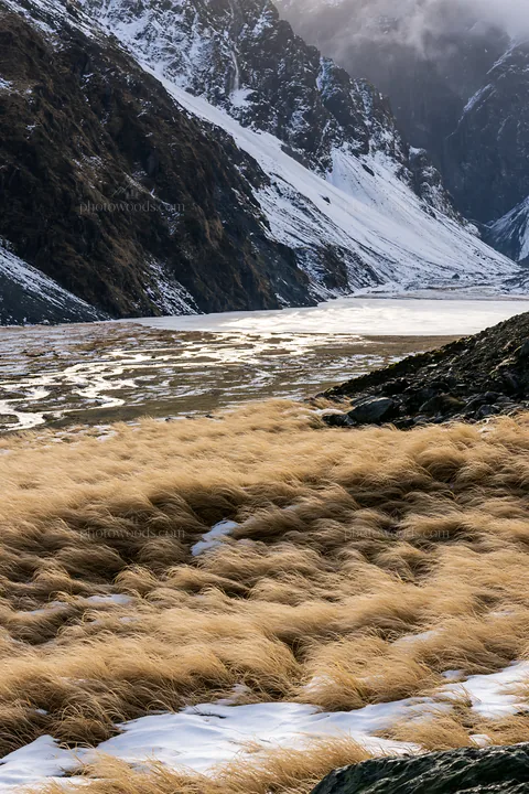 Frozen tarn meadow in mountain valley with grass and snow - AI-generated stock image