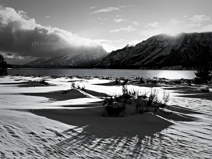 Black and white snowy lakeside meadow with mountains and sun in the background - AI-generated stock image