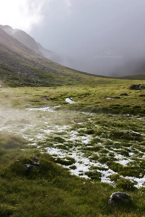 Mountain pass meadow with snow and grass in a cloudy setting - AI-generated stock image