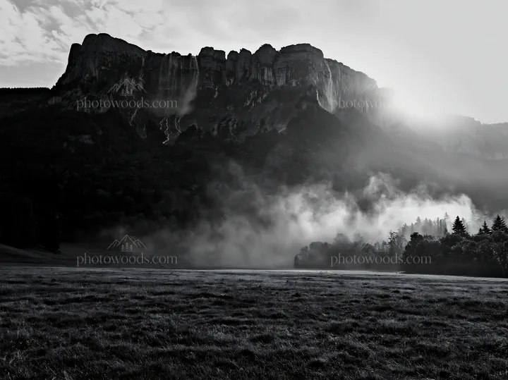 Meadow beneath crags with sunlight and mist - AI-generated stock image