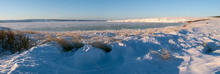 Snowy lakeside meadow with frozen water and distant hills - AI-generated stock image