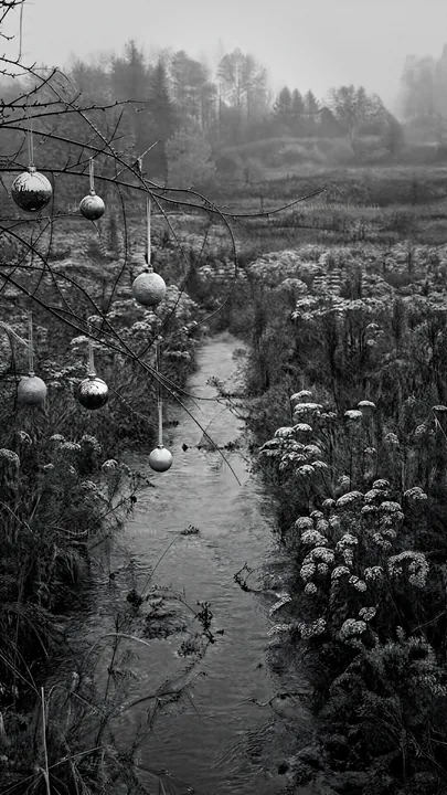 Christmas ornaments hanging above stream in meadow - AI-generated stock image