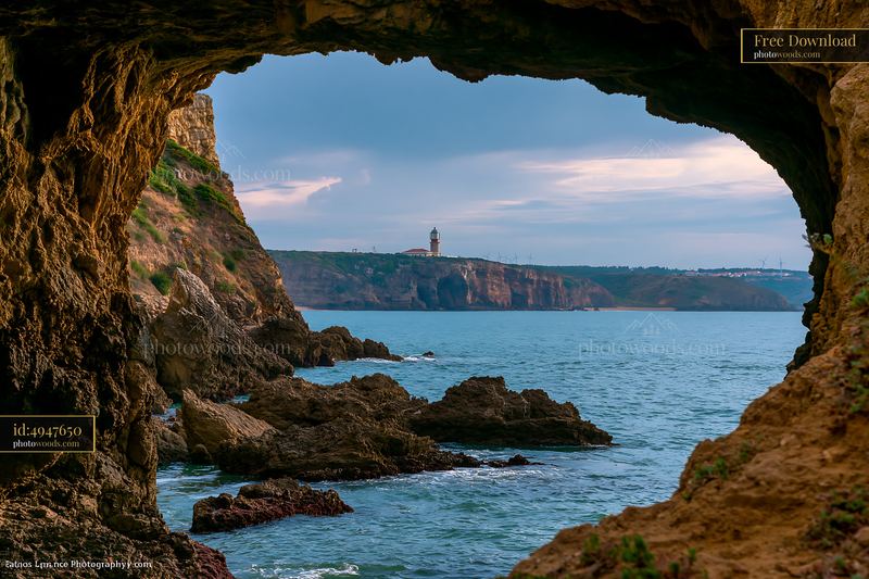 Coastline viewed through sea cave with lighthouse in distance