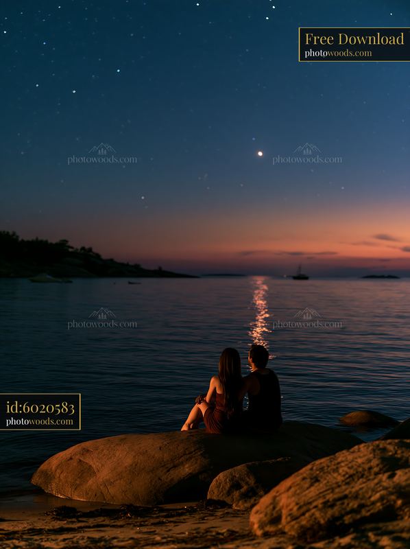 Couple sits on rocks by water under a starry night sky