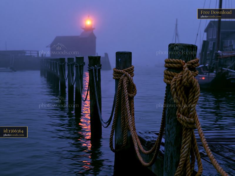 Lighthouse in heavy ocean fog with wooden posts and moored boats