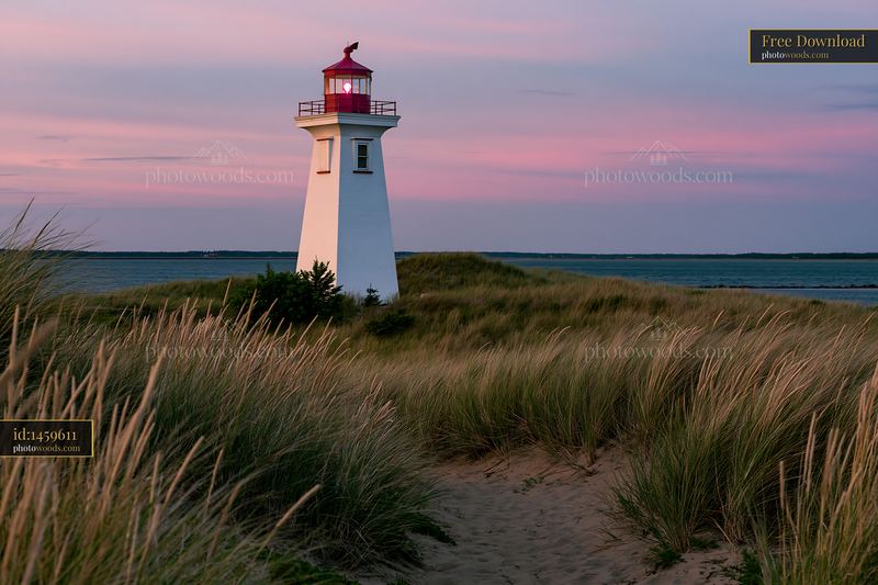 Lighthouse framed by coastal dunes during sunset