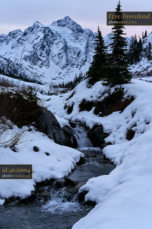 Alpine waterfall beneath snowy peaks at twilight