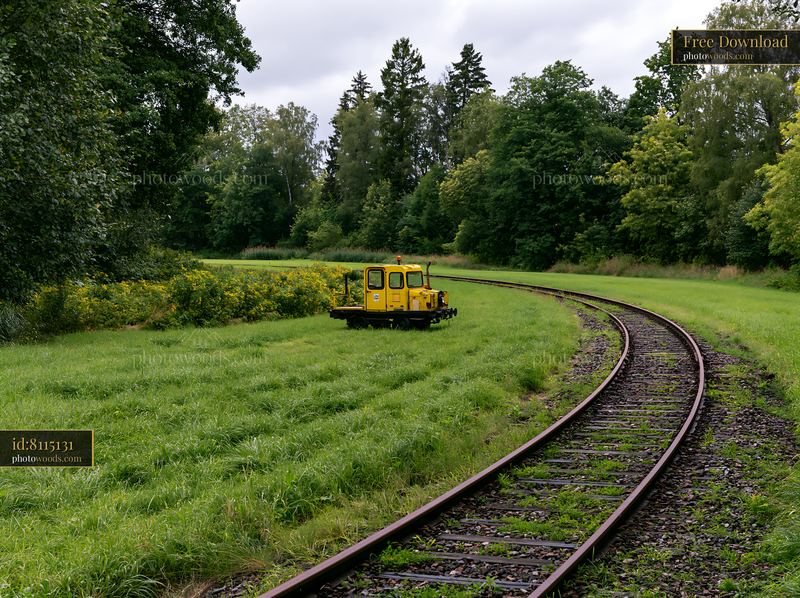 Railway tracks curve through a meadow with yellow maintenance vehicle