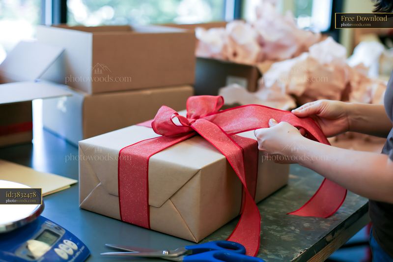 Hands tying a red ribbon around a wrapped gift box