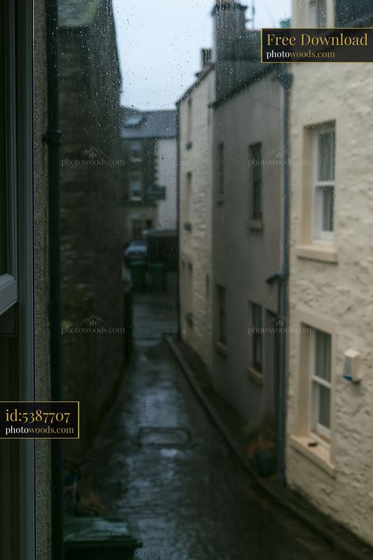 Rainy cottage exterior seen through wet glass in narrow street