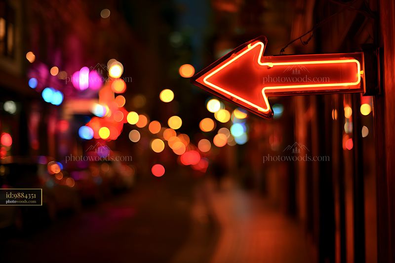 Red neon arrow sign points left on a dimly lit street