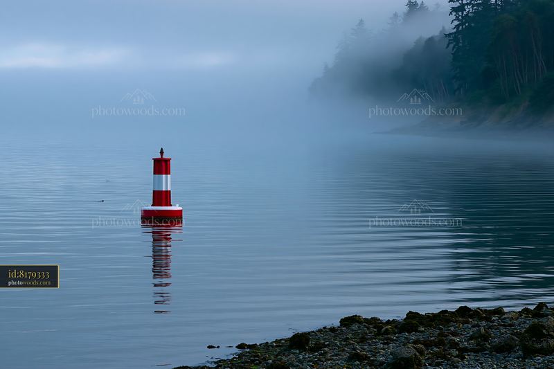 Coastline covered in sea fog near a buoy and calm water