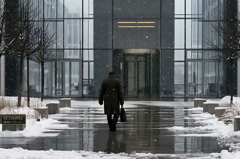Businessman walking toward modern office entrance in snowy weather