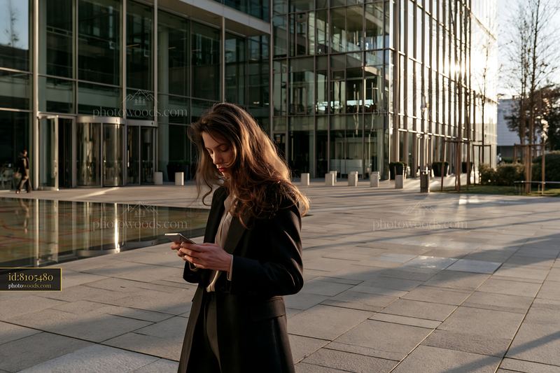 Businesswoman using smartphone outside office building during sunset