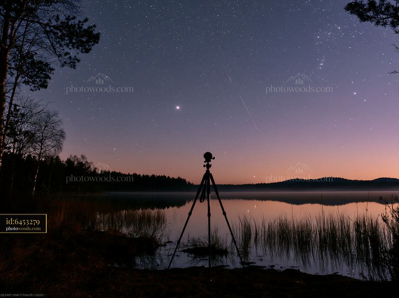 Camera tripod under stars by a calm lake at night