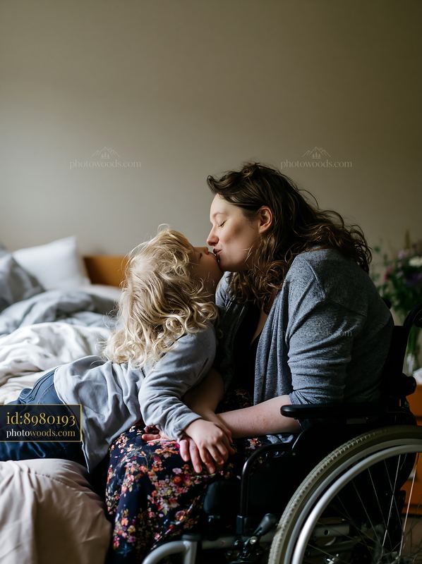 Child kissing parent in wheelchair at home