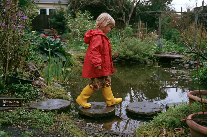 Child in yellow boots walking on stepping stones by a small pond