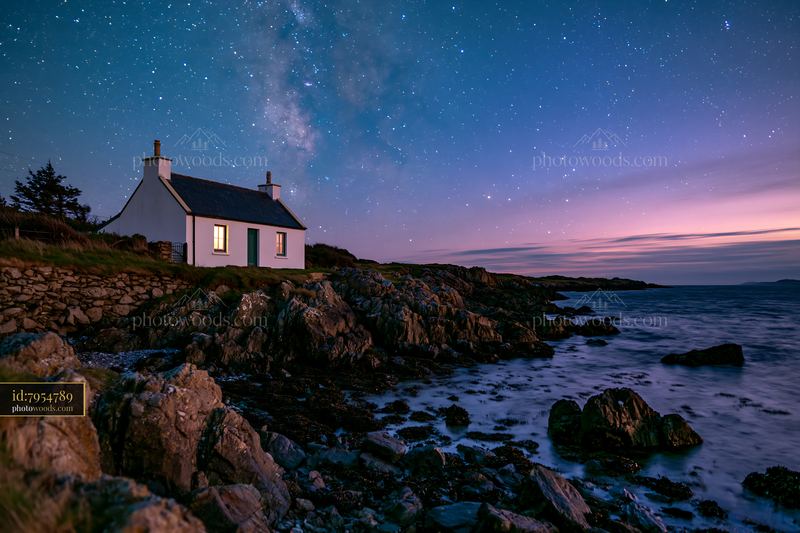 Coastal cottage under stars with rocky shoreline and sea view