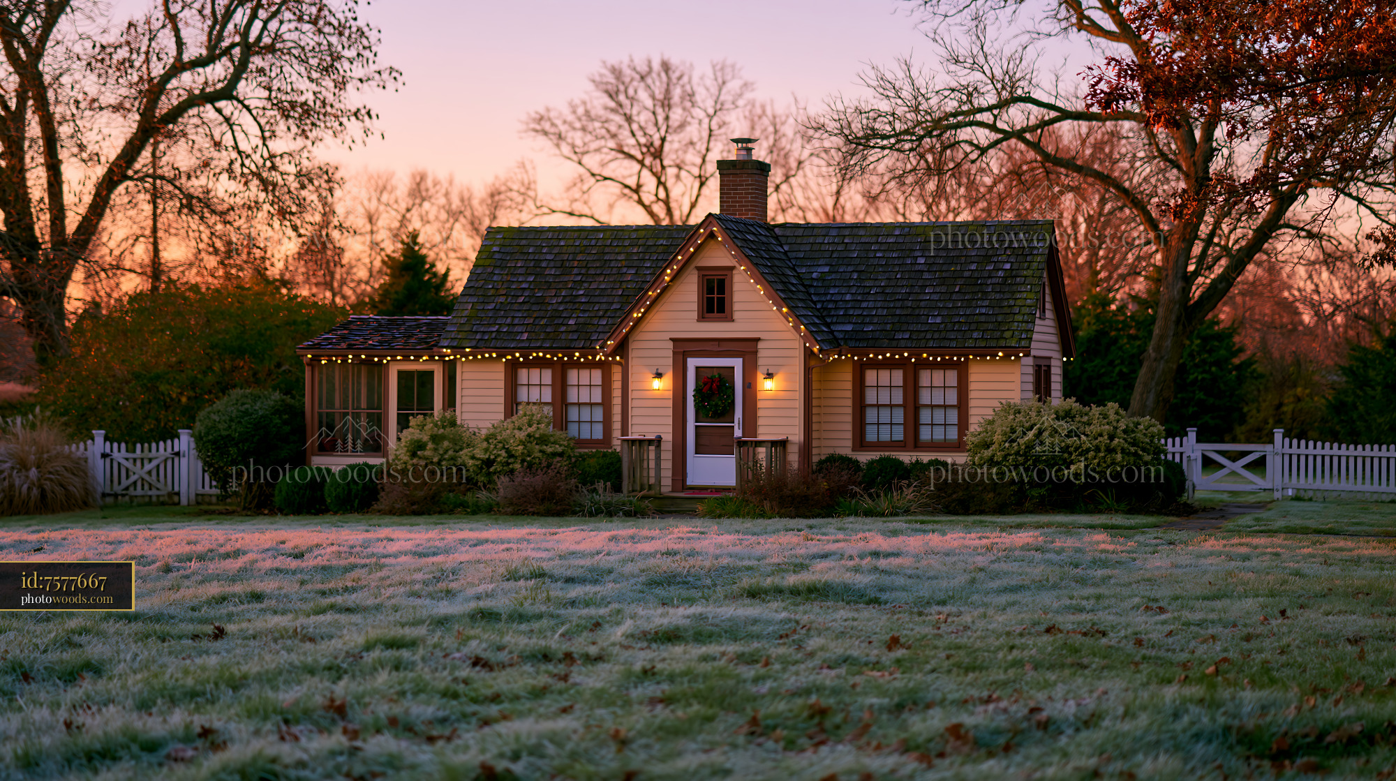 A country cottage with Christmas decorations stands in a frosty field as the sun sets.