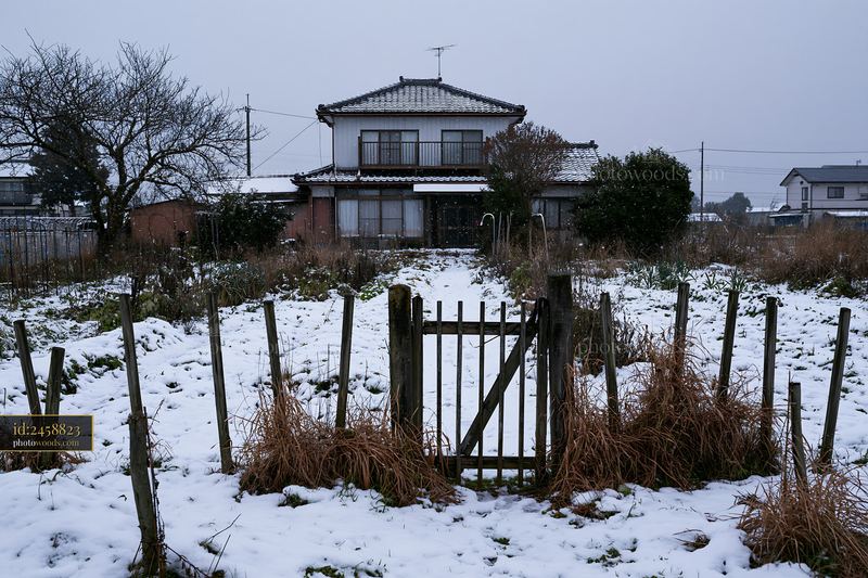 Country house under falling snow with snowy yard and fence