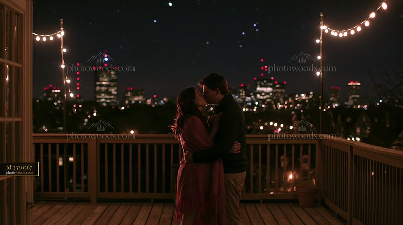 Couple kissing beneath stars while wrapped in blanket on balcony