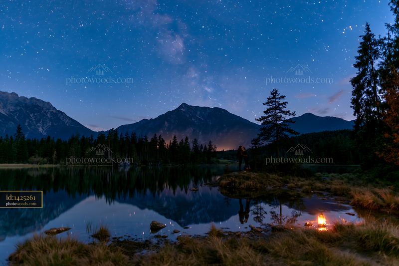 Couple kissing under stars beside a lake at night with a campfire