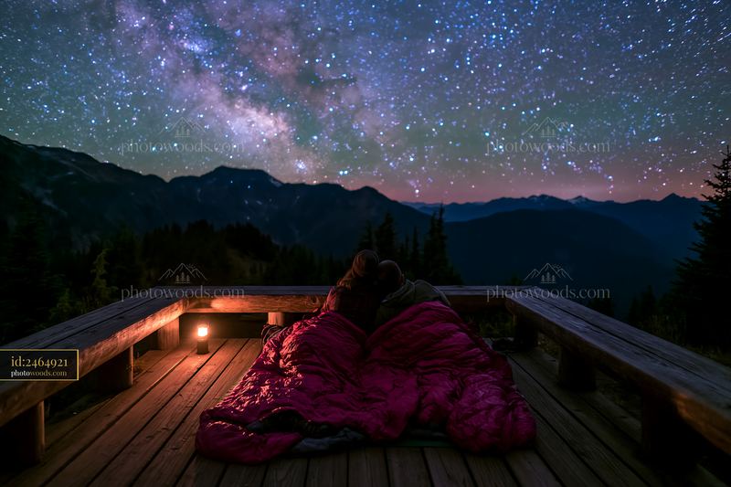 Couple sharing a sleeping bag beneath stars on a mountain deck