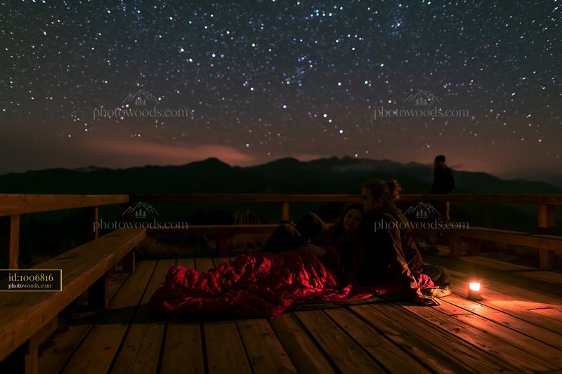 Couple sharing a sleeping bag beneath stars on a wooden deck