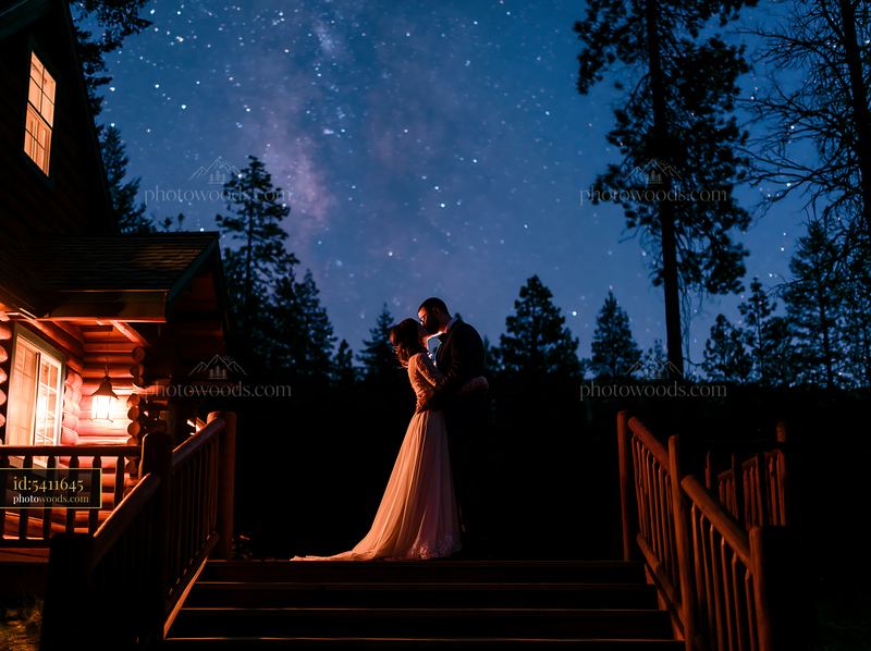 Newlyweds kiss outdoors beneath stars near a rustic cabin