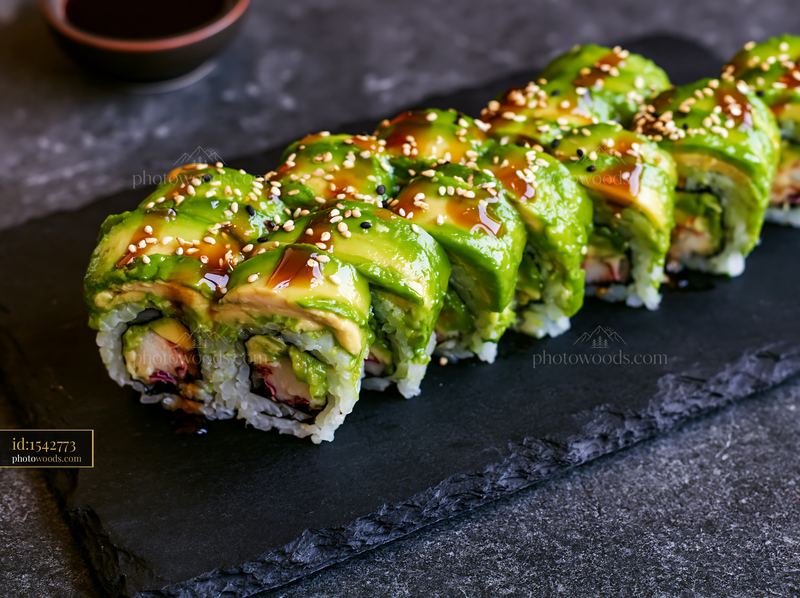 Dragon roll close-up with avocado and sauce on a dark plate