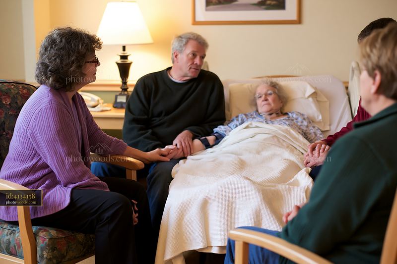 Family holding hands beside hospice patient in a cozy room