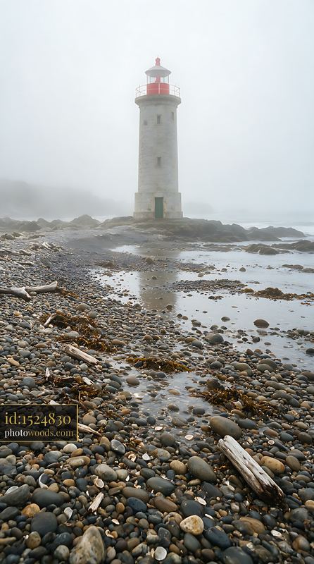 Lighthouse standing in heavy ocean fog by rocky shore