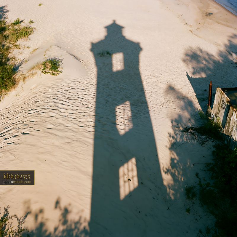 Lighthouse shadow on sandy beach under dramatic clouds