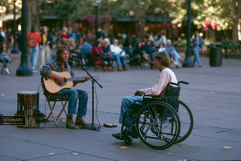 Musician plays guitar for person in wheelchair in public square