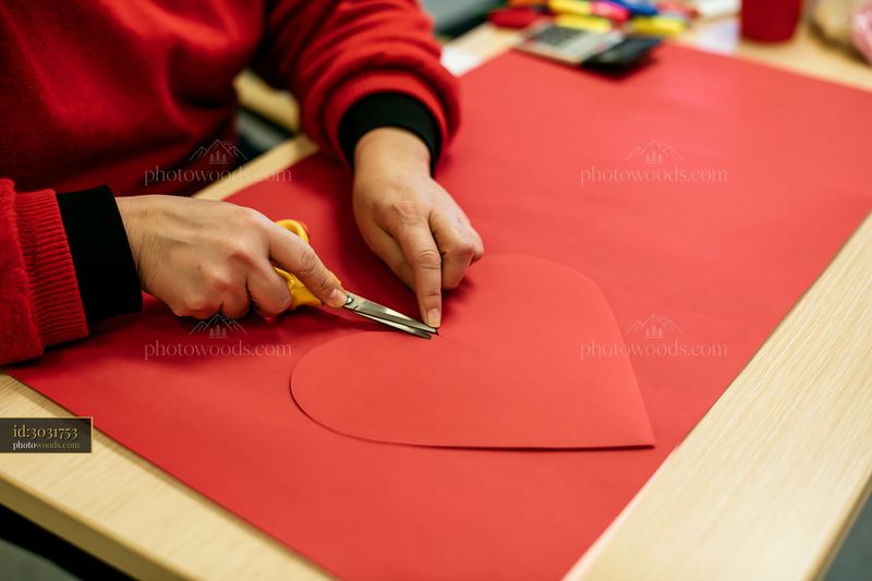Hands cutting a heart shape from red paper for craft project