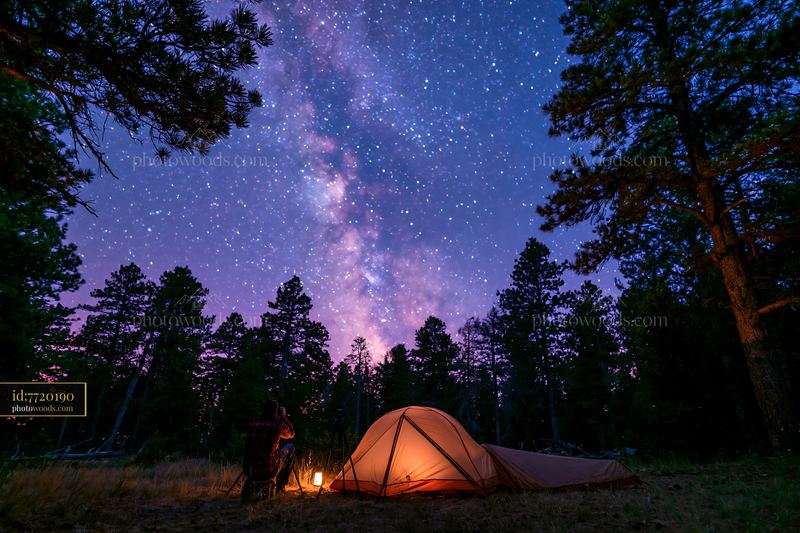 Person photographing stars at night with a tent and campfire