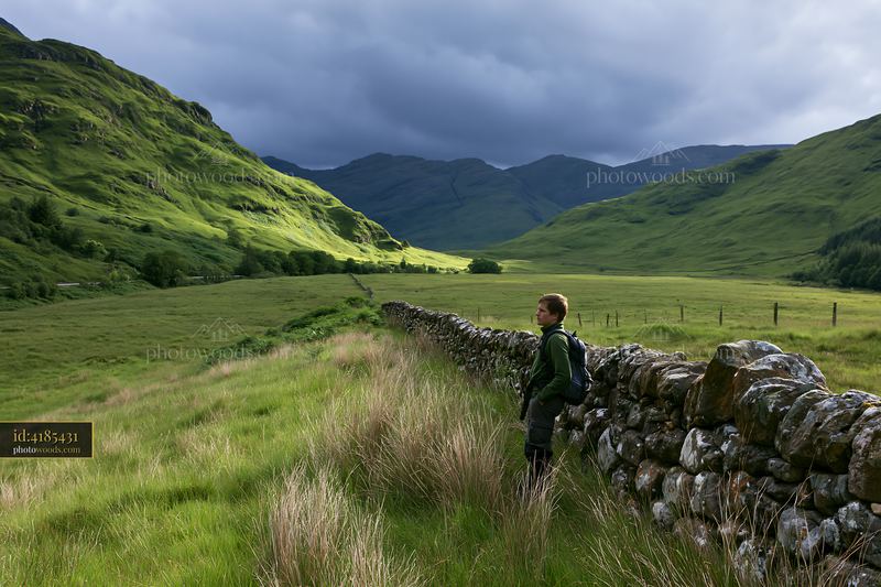 Stormy highland valley with a person by a stone wall