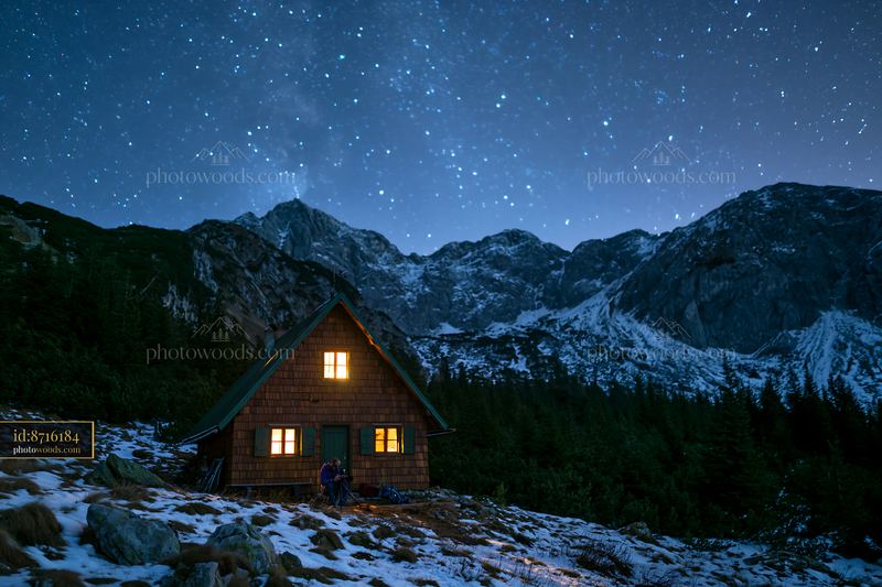 Photographer under stars in the mountains near a cabin