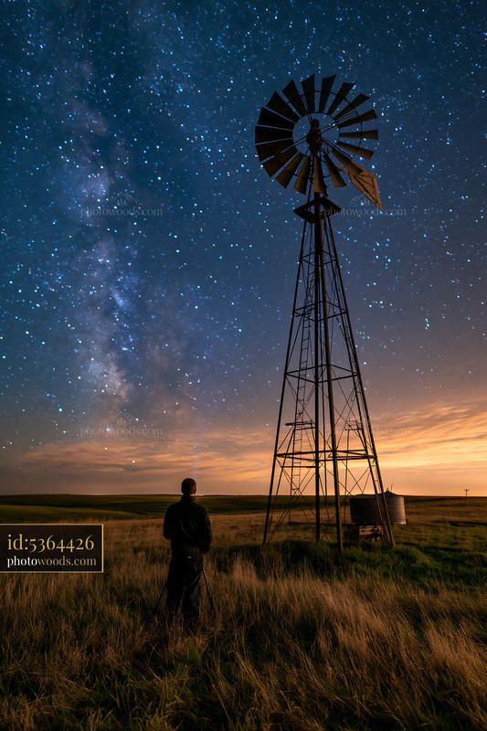 Photographer under stars near a windmill in a night scene