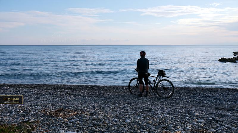 Bicyclist at pebbly coastline beach by calm waters