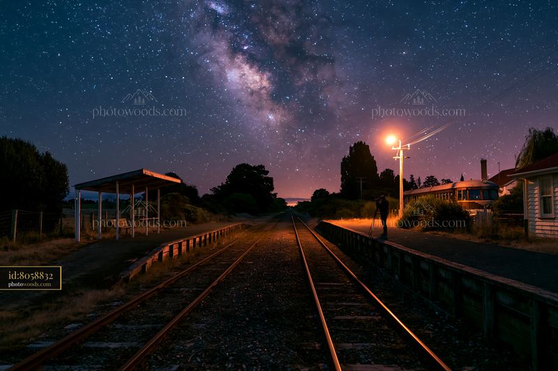 Person using camera under Milky Way at train tracks