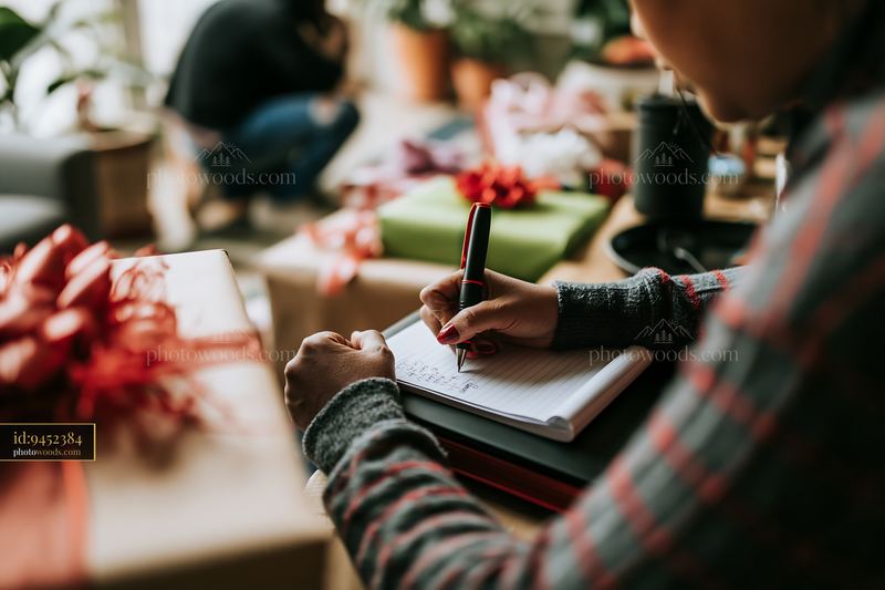 Person writing a gift list at desk with wrapped presents nearby